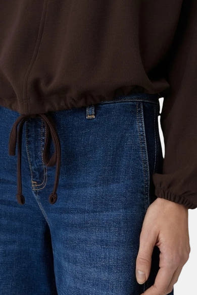 Sweat col rond brun de OPUS, avec cordon de serrage assorti à la taille, porté avec un jean bleu.
