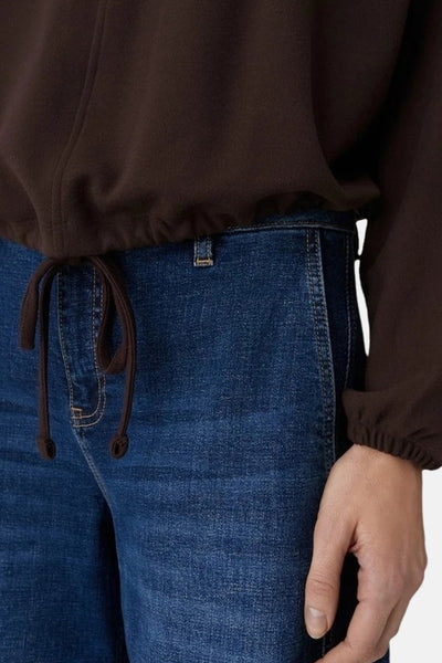 Sweat col rond brun de OPUS, avec cordon de serrage assorti à la taille, porté avec un jean bleu.
