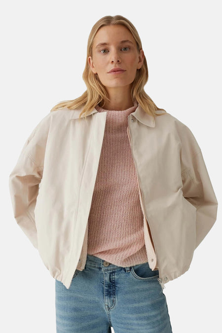 Veste courte beige de OPUS, portée avec un pull rose en maille et un jean bleu classique.