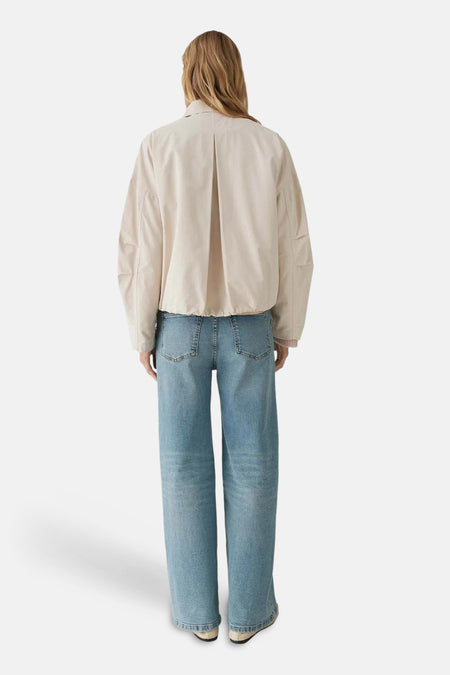 Veste courte beige de OPUS, avec pli creux au dos, portée avec un jean ample bleu clair.