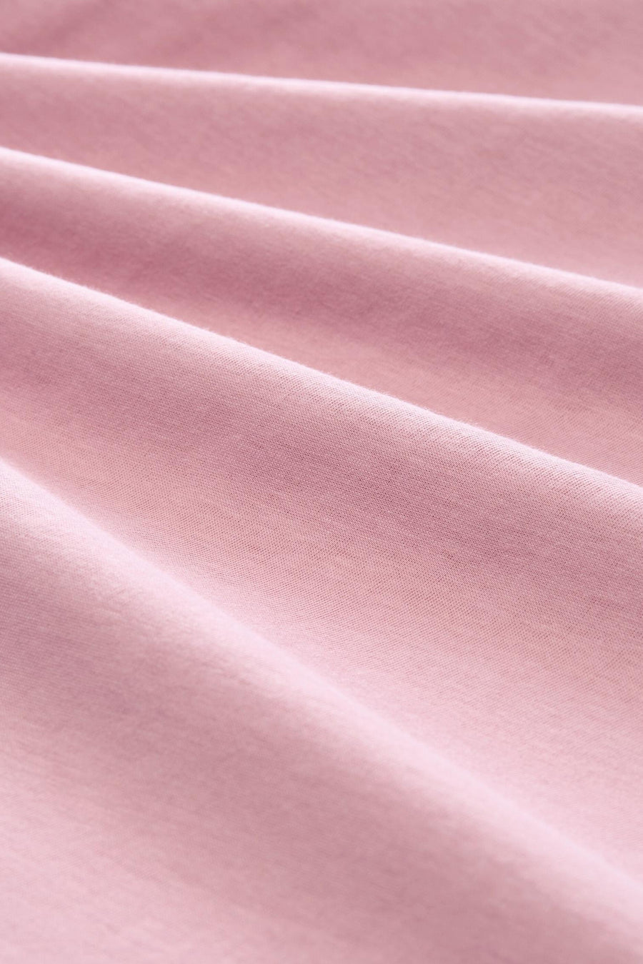 Soft pink short-sleeve t-shirt fabric close-up, smooth texture with gentle folds, solid color, soft cotton material.