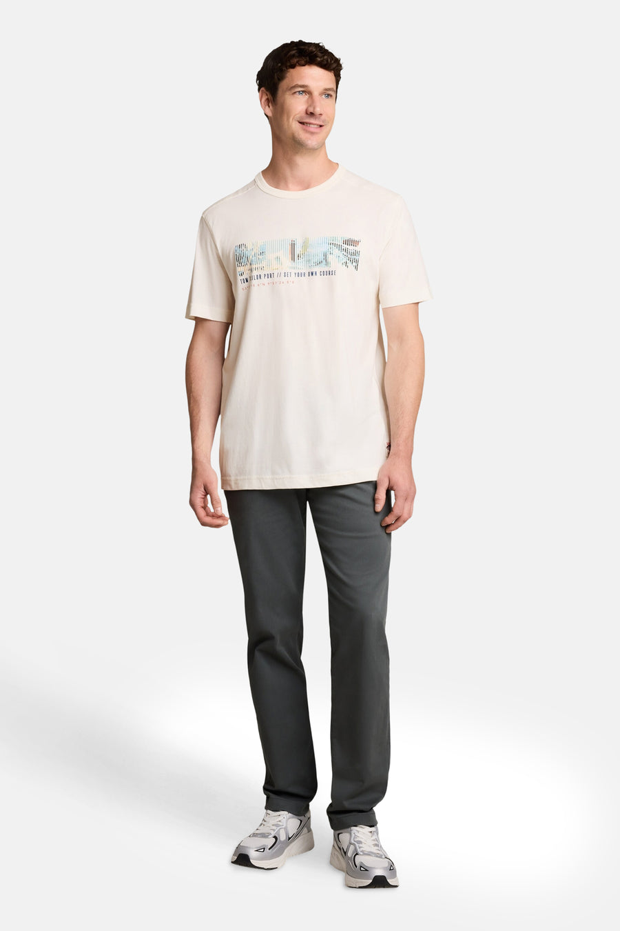 Off-white short-sleeve t-shirt with colorful pixelated graphic and text, worn by model in full-length lifestyle view with dark pants and sneakers.