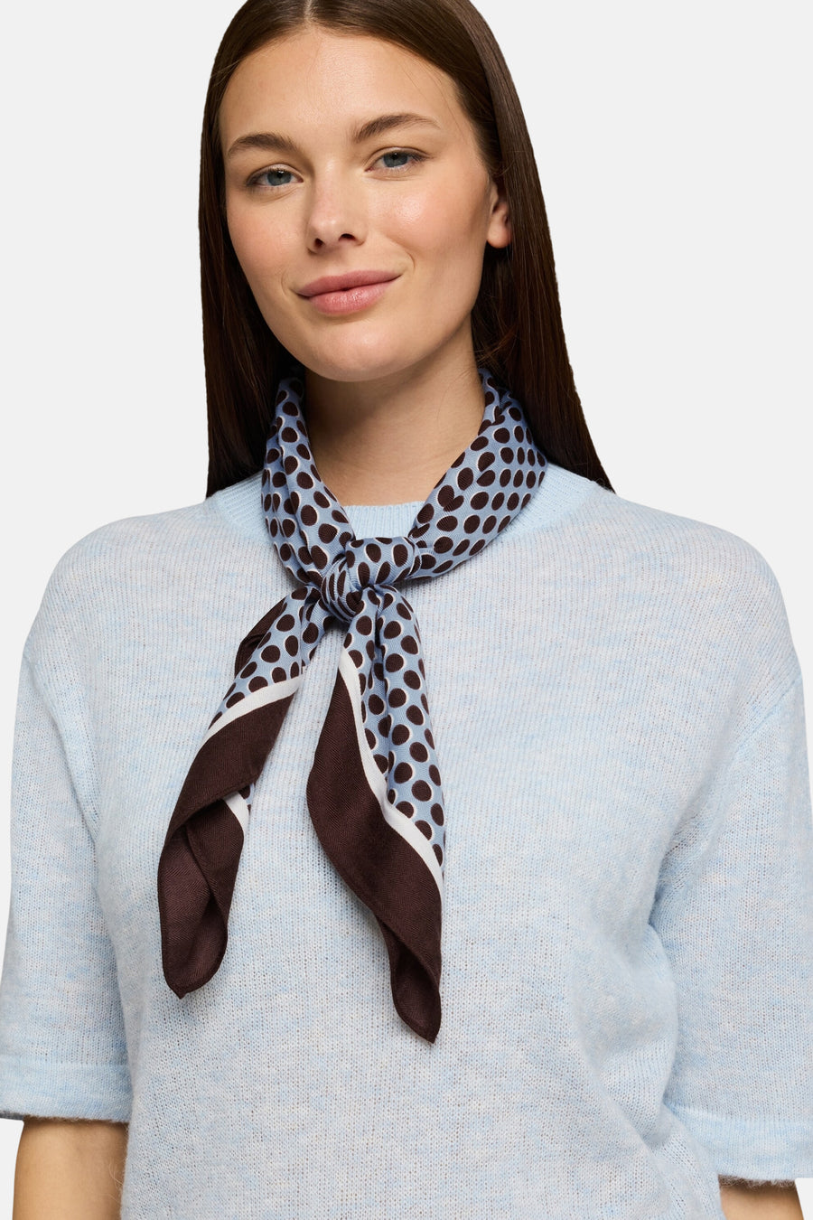 Multicolored polka dot scarf by Tom Tailor, tied in a knot, featuring brown and light blue pattern, worn with light blue knit top, front view.