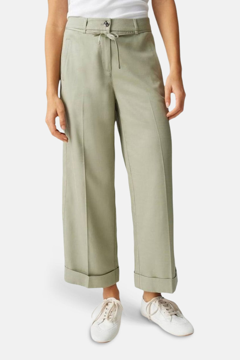 Pantalon de costume vert par OPUS, jambe large et revers aux chevilles, porté avec un t-shirt blanc et des chaussures de sport.