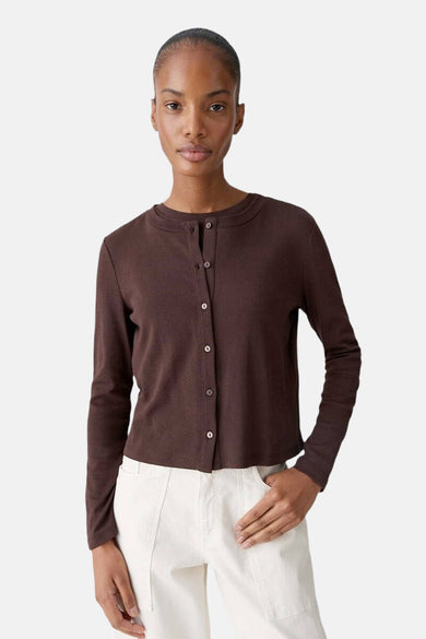 Cardigan brun de OPUS, boutonné sur le devant, porté avec un pantalon écru.
