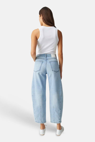 Jean large en denim bleu clair OPUS porté de dos par une femme avec un débardeur blanc et des baskets blanches.