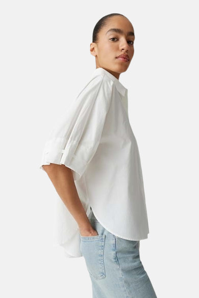 Chemise blanche à manches courtes d'OPUS, coupe ample avec patte sur les manches, portée avec un jean bleu clair.