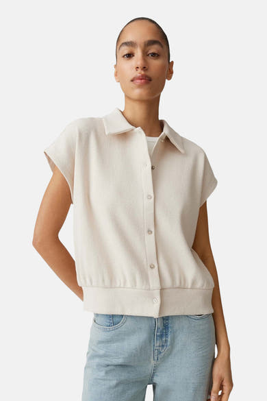 Pull col V beige de OPUS à la texture gaufrée, manches courtes et col chemise, porté avec un jean clair.