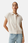 Pull col V beige de OPUS à la texture gaufrée, manches courtes et col chemise, porté avec un jean clair.