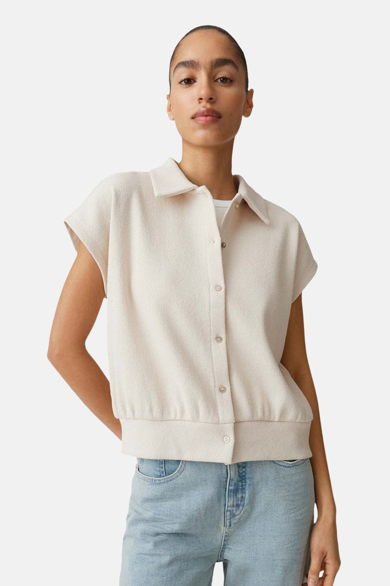 Pull col V beige de OPUS à la texture gaufrée, manches courtes et col chemise, porté avec un jean clair.
