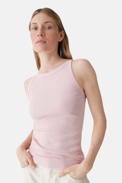 Débardeur rose côtelé de OPUS, porté par une femme les mains dans les poches de son pantalon blanc.