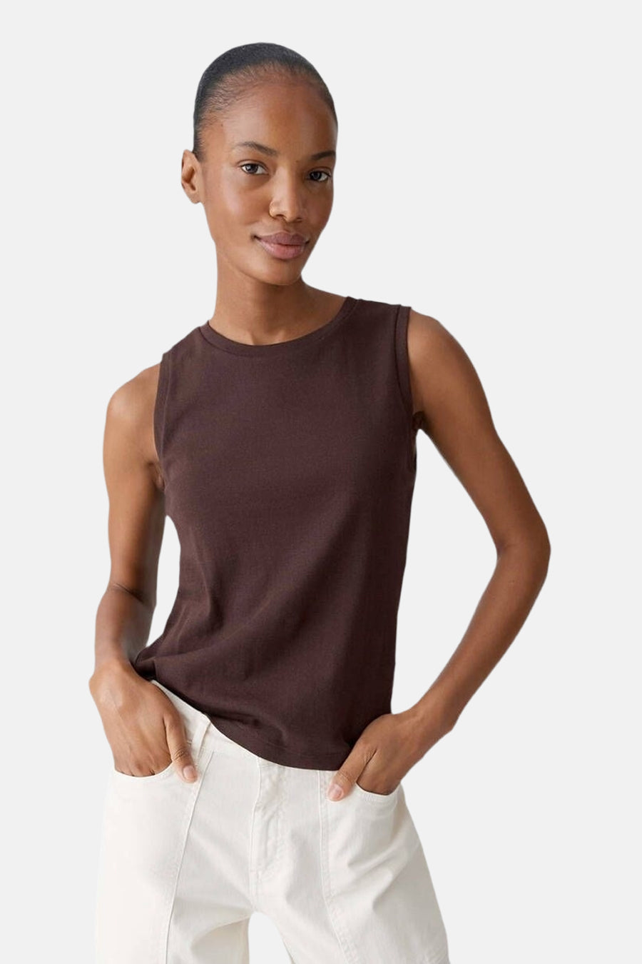 Top sans manches brun, par OPUS, porté avec un pantalon blanc à poches, devant un fond neutre.