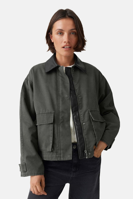 Oversized green parka with front zipper and flap pockets, worn over a white top and dark jeans, front view.