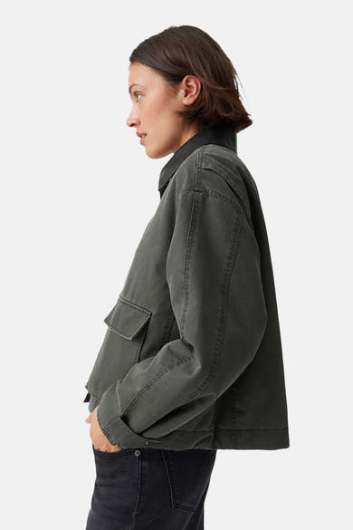 Olive green parka with black collar and side pockets, side view, worn with dark jeans
