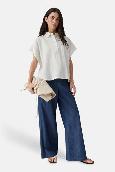 White sleeveless blouse with button front and relaxed fit, worn with wide-leg denim pants and sandals, full-body lifestyle view