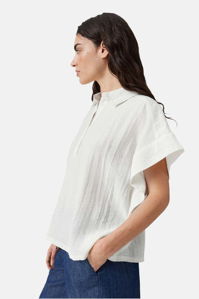 White sleeveless blouse with button placket and relaxed fit, side view on model wearing blue jeans