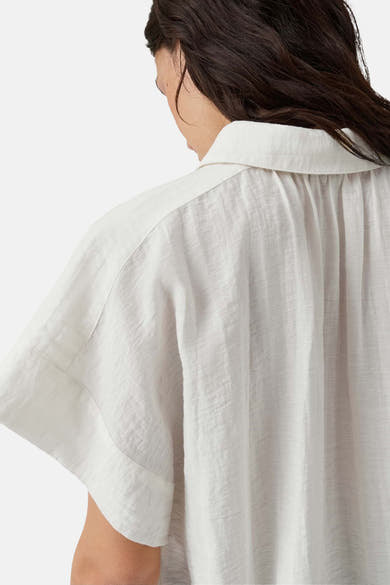 White sleeveless blouse with relaxed fit and textured fabric, back view showing collar and gathered shoulders