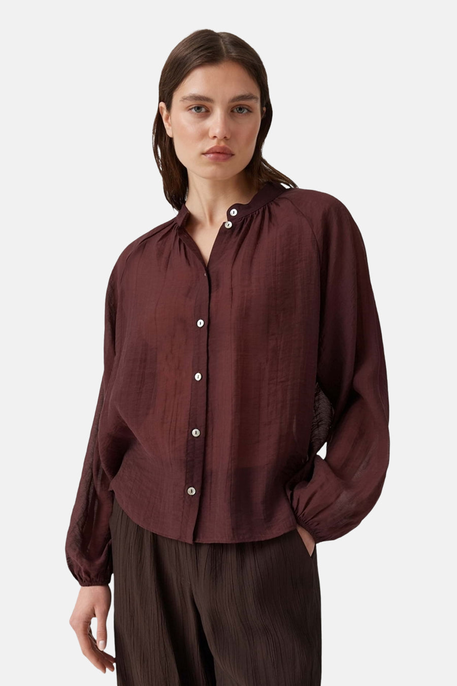 Bordeaux long-sleeve blouse with gathered neckline and white buttons, featuring a relaxed fit and textured fabric, front view on model wearing dark pleated trousers