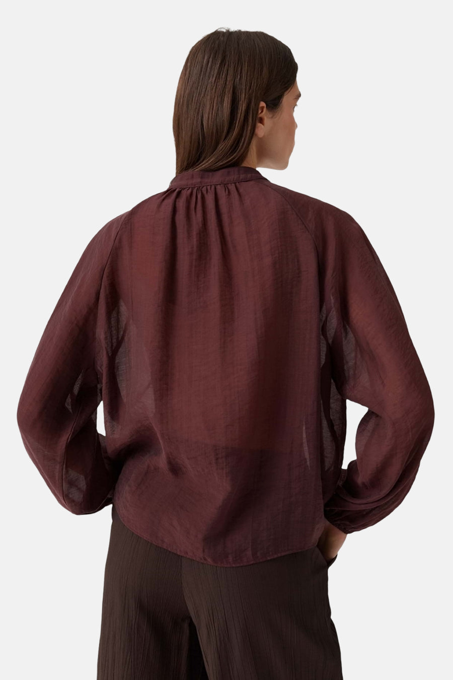 Bordeaux long-sleeve blouse with gathered neckline and sheer fabric, back view, worn with dark pleated trousers