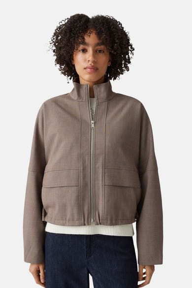 Taupe bomber jacket with front zip and two patch pockets, worn over white ribbed top and dark jeans, front view.
