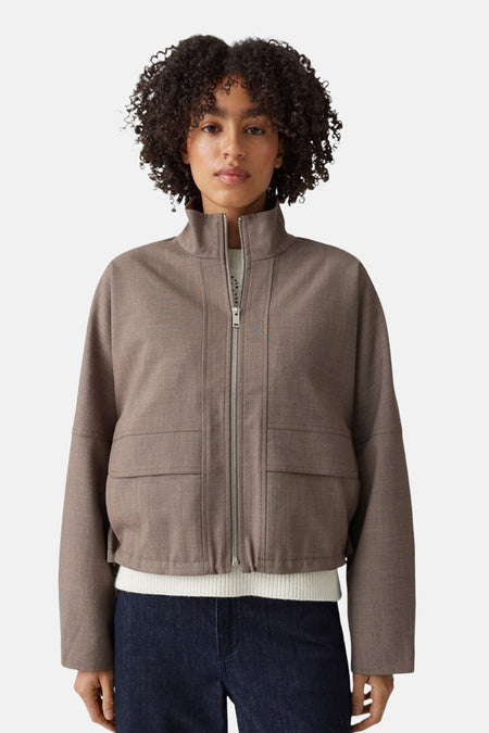 Taupe bomber jacket with front zip and two patch pockets, worn over white ribbed top and dark jeans, front view.