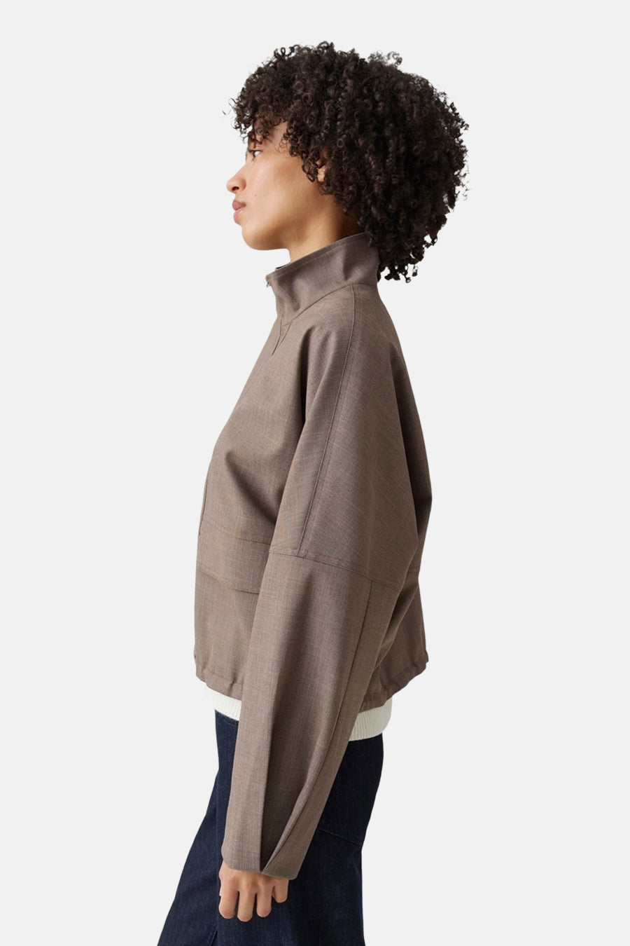 Kaki brown bomber jacket by [brand omitted] in textured fabric, side view, cropped fit with ribbed hem and stand-up collar, worn with white ribbed top and dark jeans.