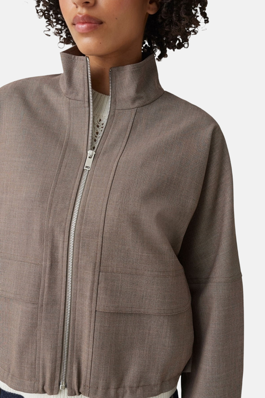 Taupe bomber jacket with high collar and front zipper, featuring textured fabric and two front pockets, worn over a white ribbed top in a cropped front view.