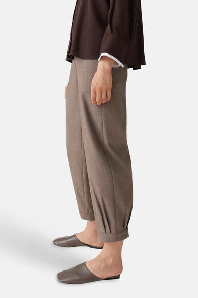 Brown chino pants with cuffed hems and relaxed fit, side view on model wearing dark top and slip-on shoes