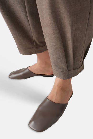 Brown chino pants with cuffed hems and subtle texture, worn with matching slip-on mules, side view.