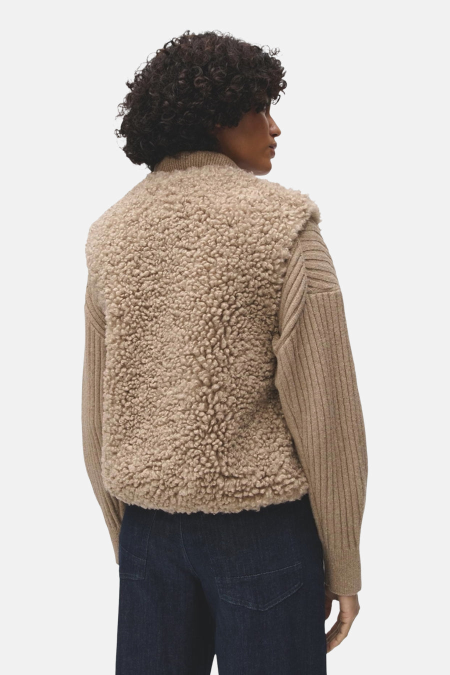 Dos d’une personne portant une veste sans manches beige en matière bouclée, avec col montant et poches passepoilées.
