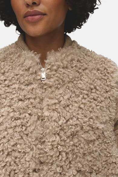 Gros plan sur une veste sans manches beige à col montant et fermeture zippée, portée par un mannequin.