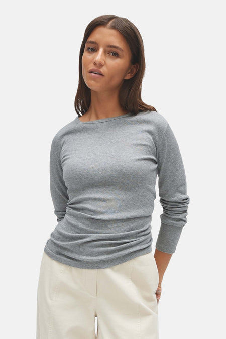 Top gris uni à manches longues de OPUS, en maille douce, porté avec un pantalon blanc, vue de face.