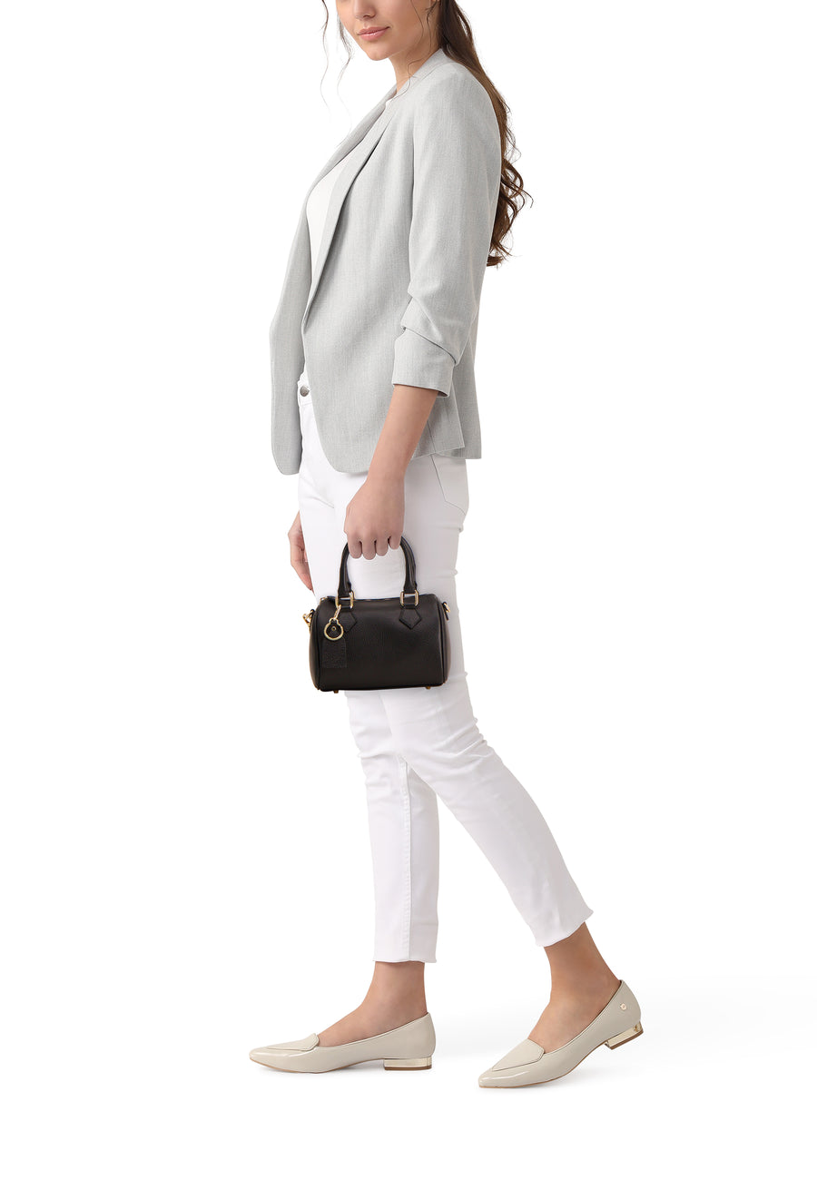 Sac à main noir d'Access® avec poignées et détails dorés, porté par une femme en tenue chic décontractée.