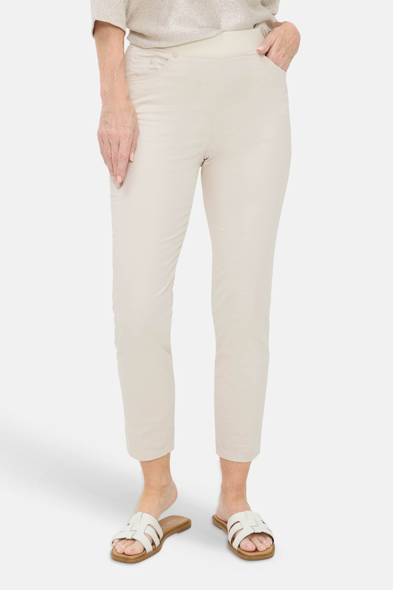 Beige slim-fit jeans by PAMINA 68, front view, cropped at ankles, worn with beige top and white sandals