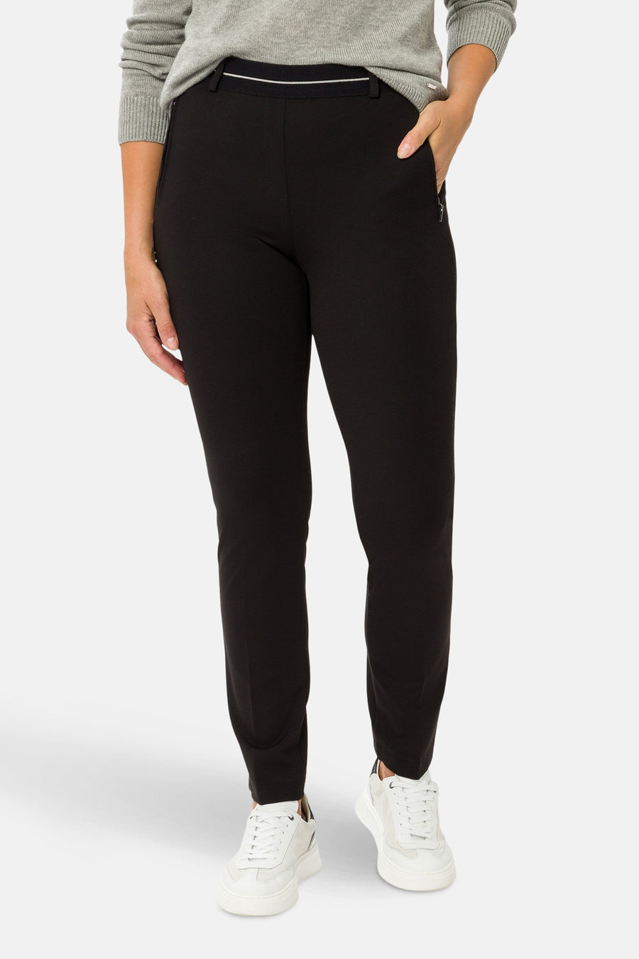 Zwarte broek van RAPHAELA, met ritszakken en een witte bies aan de taille, gedragen met een grijze trui.