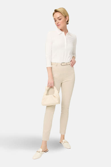 Pantalon de costume écru de RAPHAELA, porté avec une ceinture et un haut blancs, et des mules.
