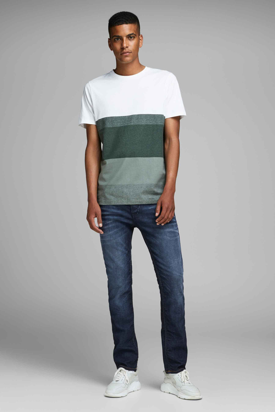 Slim jeans in donkerblauw denim van JACK & JONES JEANS INTELLIGENCE, gedragen met een gestreept T-shirt en witte sneakers.