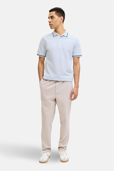 Polo bleu à manches courtes de PREMIUM by JACK & JONES, avec des bordures marine, porté avec un pantalon beige et des baskets blanches.