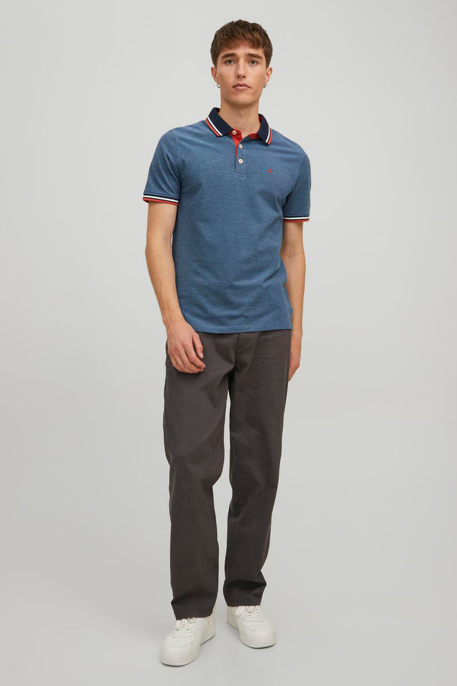 Gemêleerd blauw poloshirt van PREMIUM by JACK & JONES, met rood-witte gestreepte kraag en mouwen, gedragen met een grijze broek.