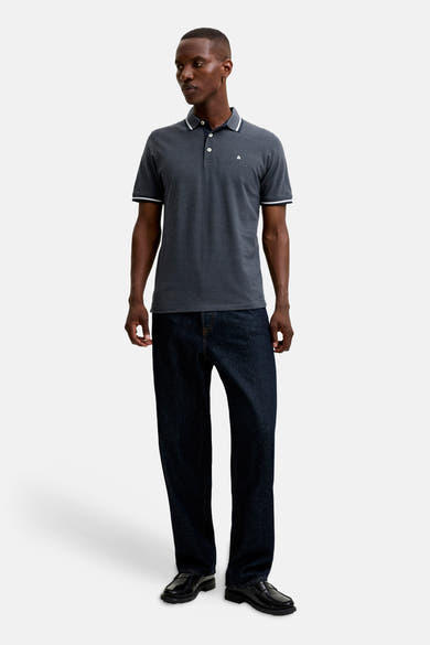 Navy blue polo shirt with white trim on collar and sleeves, featuring small logo on chest, worn by model in full-length lifestyle view with dark jeans and black loafers.
