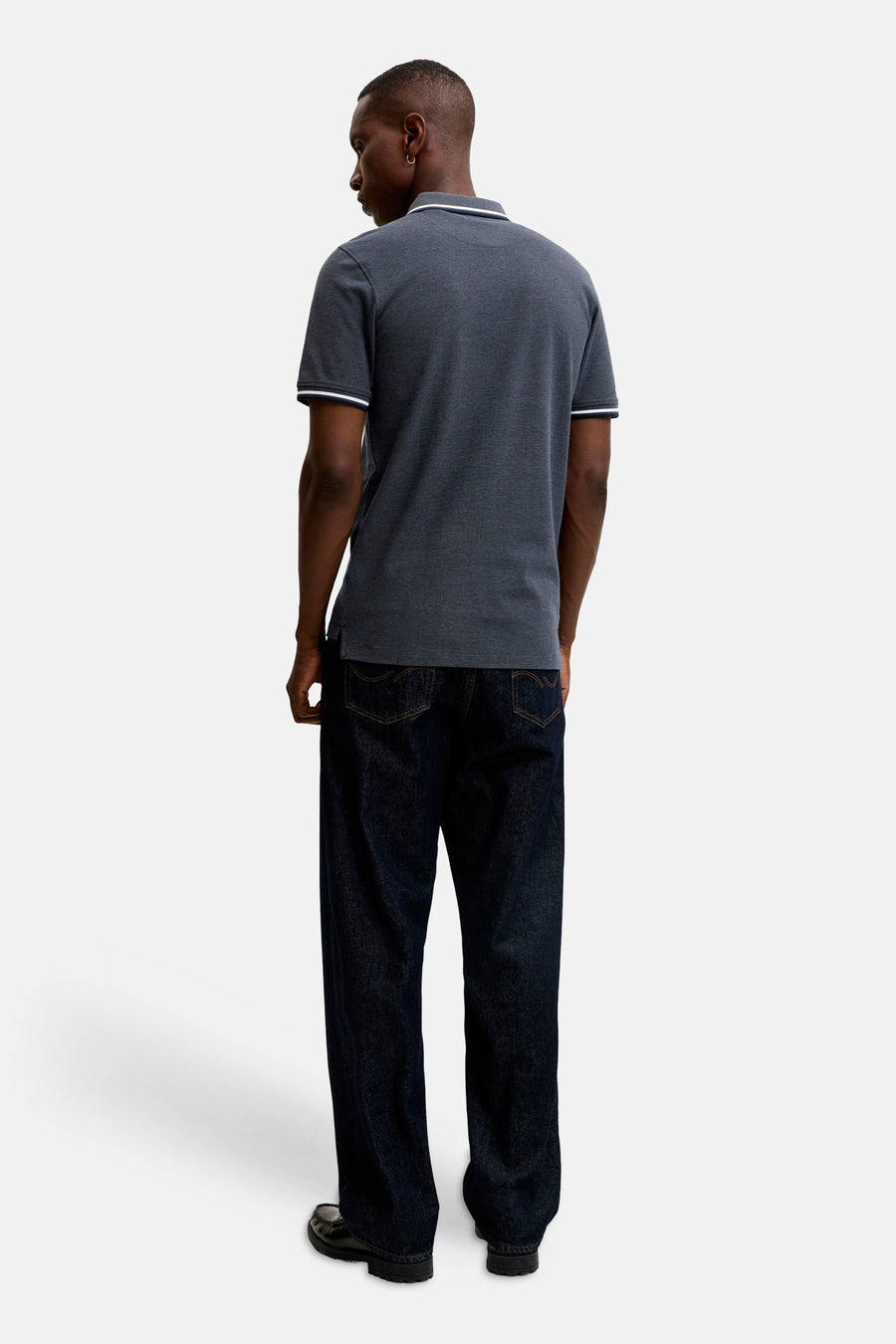Blue polo shirt with white-trimmed collar and sleeves, back view, worn with dark jeans and black loafers.