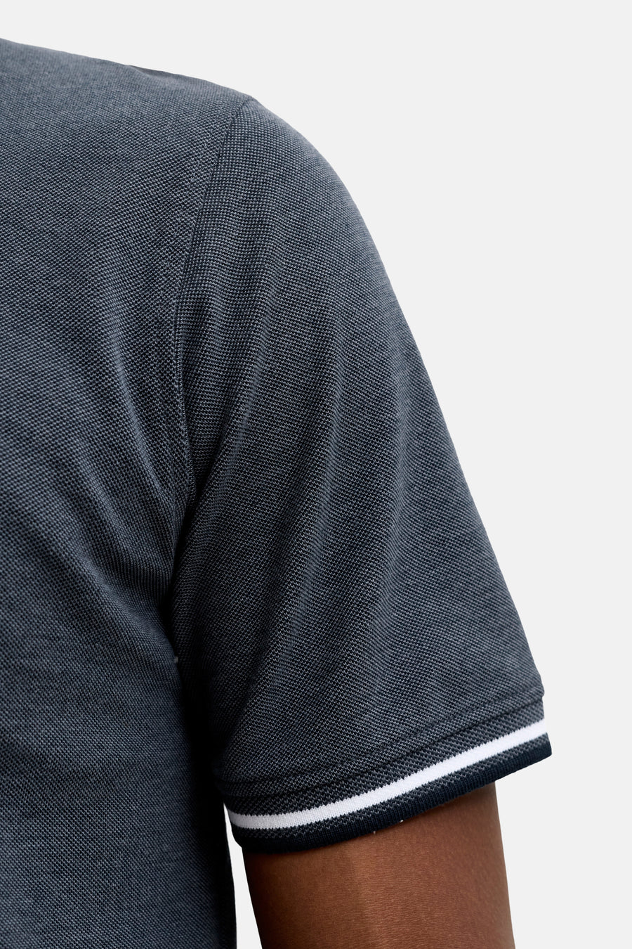 Navy blue polo shirt with textured piqué fabric and white trim on sleeve cuff, side view close-up
