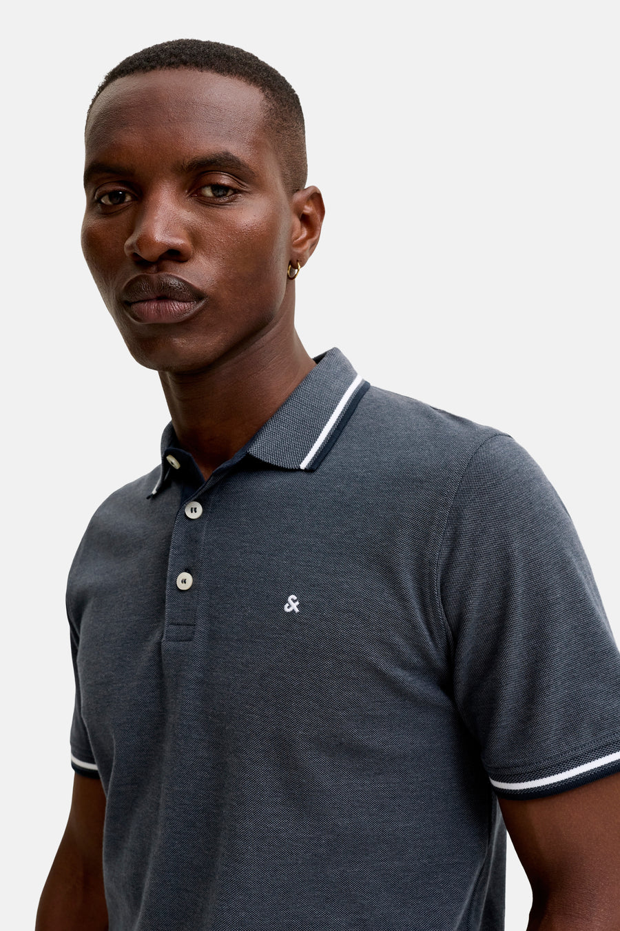 Navy blue piqué polo shirt with white contrast trim on collar and cuffs, featuring a small white ampersand logo on chest, worn by model in front view.