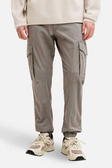 Pantalon cargo brun de JACK & JONES JEANS INTELLIGENCE avec des poches cargo et des ourlets élastiques, porté avec des baskets beiges.