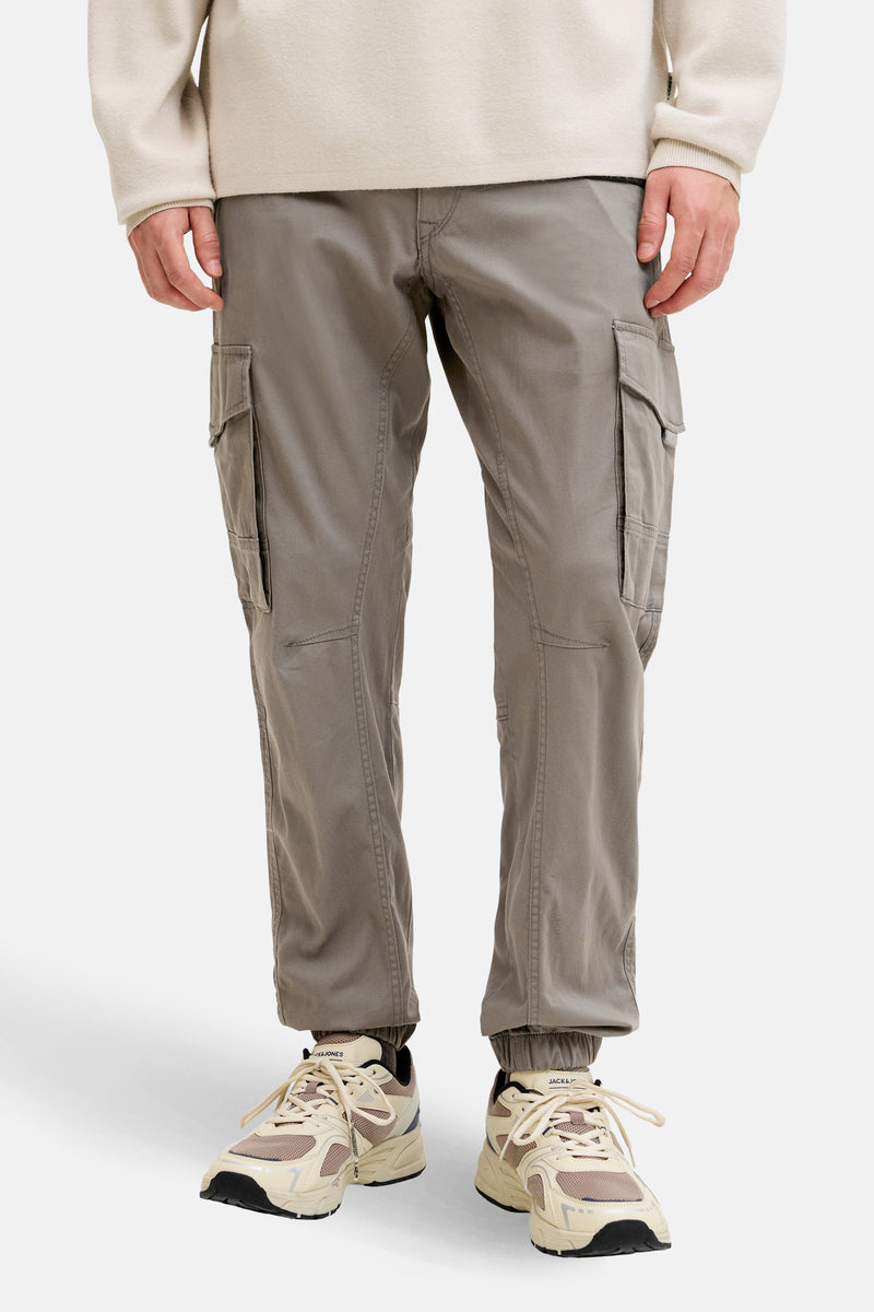 Pantalon cargo brun de JACK & JONES JEANS INTELLIGENCE avec des poches cargo et des ourlets élastiques, porté avec des baskets beiges.