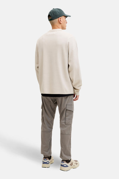 Pantalon cargo brun de JACK & JONES JEANS INTELLIGENCE avec poches latérales, porté avec un pull beige et des chaussures de sport.