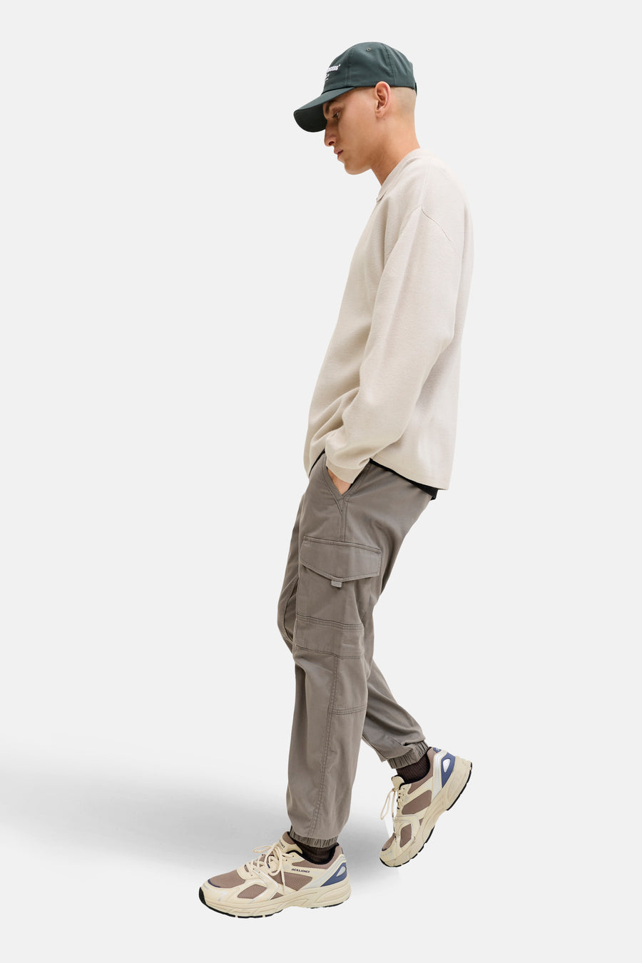 Bruine cargobroek van JACK & JONES, met zakken en nauwsluitende onderkant, gedragen met een beige trui en een groene pet.