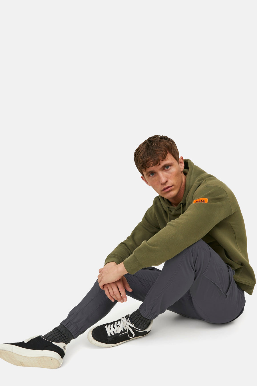 Grijze chino van JACK & JONES JEANS INTELLIGENCE, gedragen met een groene hoodie en zwart-witte sneakers.