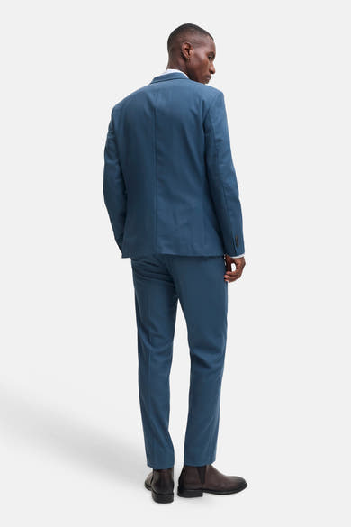 Blue tailored suit pants by JACK & JONES, shown from back view with matching blazer, slim fit, smooth texture, and dark brown boots.