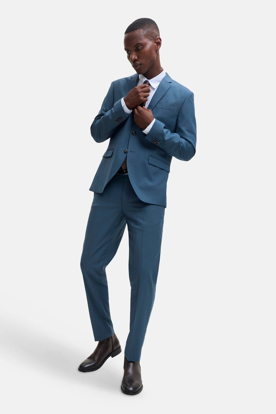 Blue slim-fit suit trousers by JACK & JONES, worn with matching blazer, white shirt, and brown leather boots in full-length lifestyle pose.